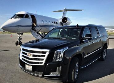 Black Cadillac Escalade parked beside a private jet